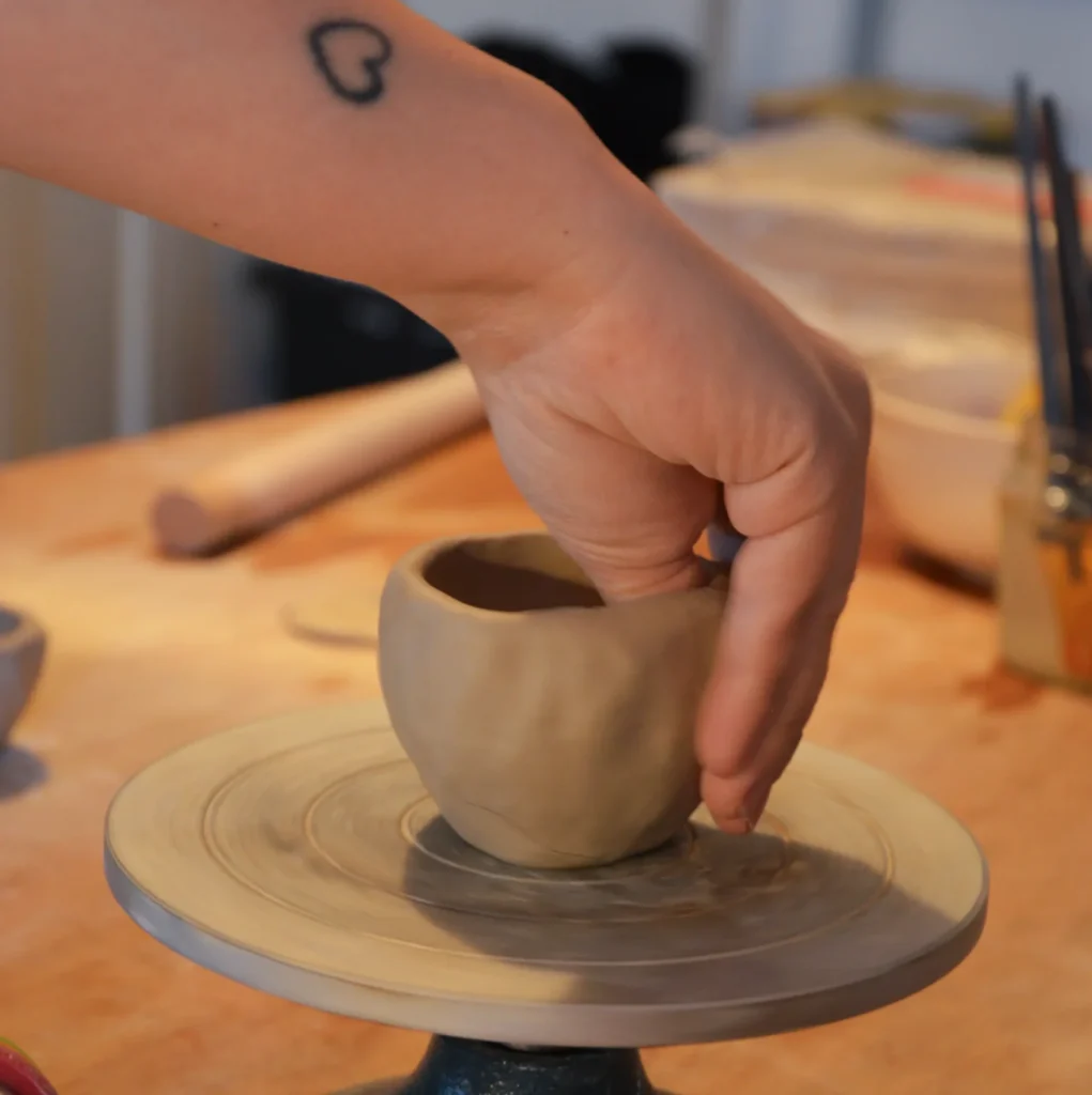 Main d'adulte affinant les bords d'une petite tasse en argile crue sur tournette en atelier céramique
