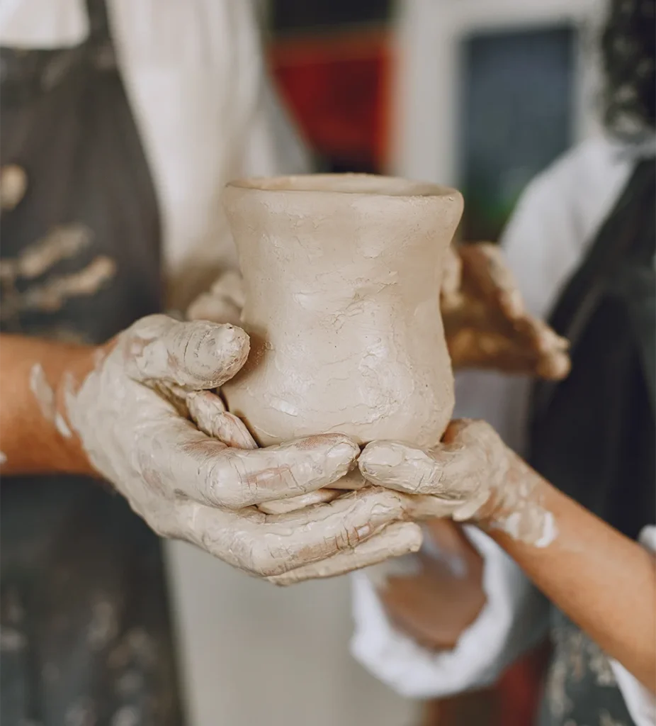 Deux paires de mains façonnant ensemble une pièce en argile lors d'un atelier de modelage